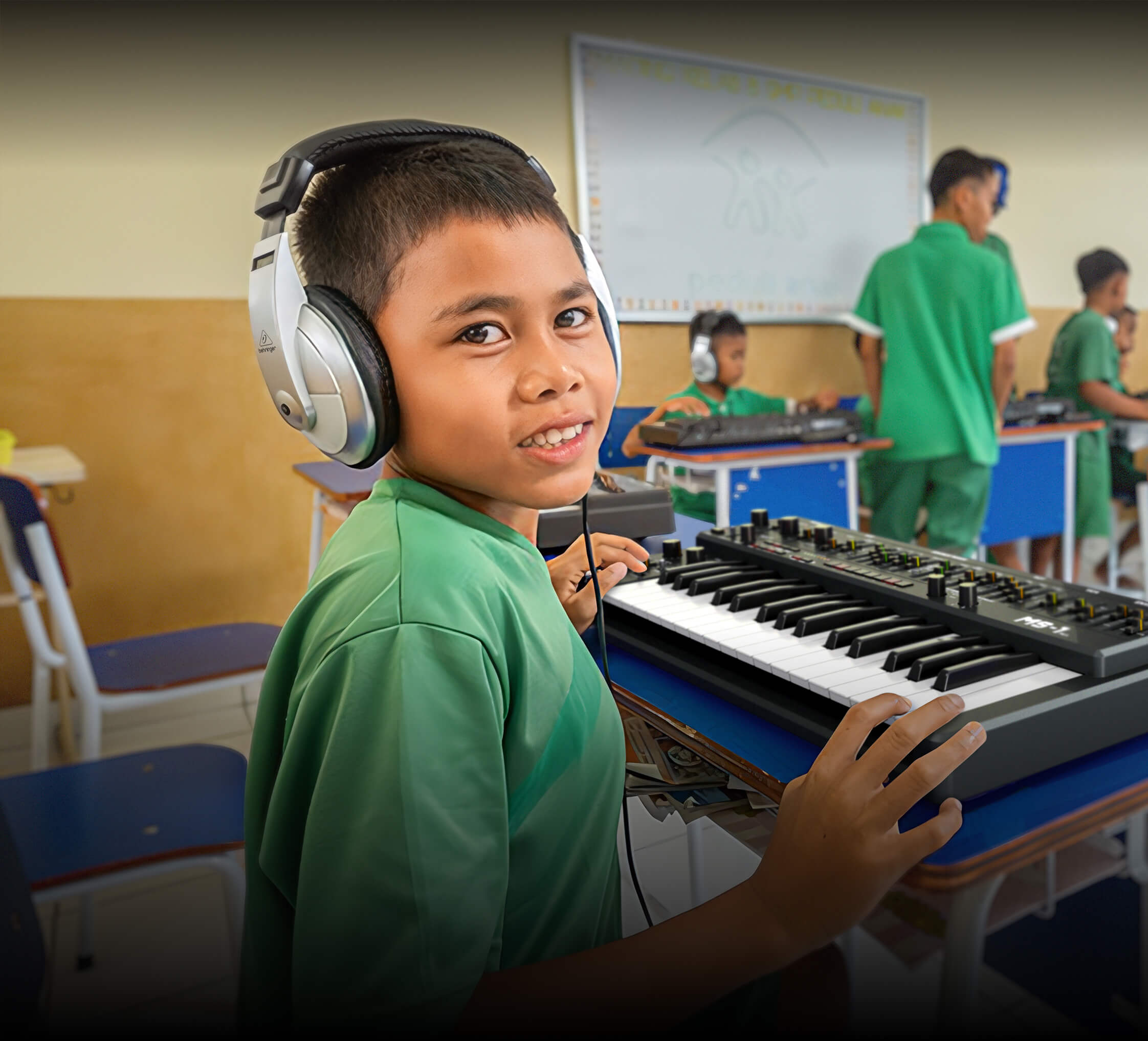 A young creator in a music-education classroom, smiling at a keyboard while wearing headphones